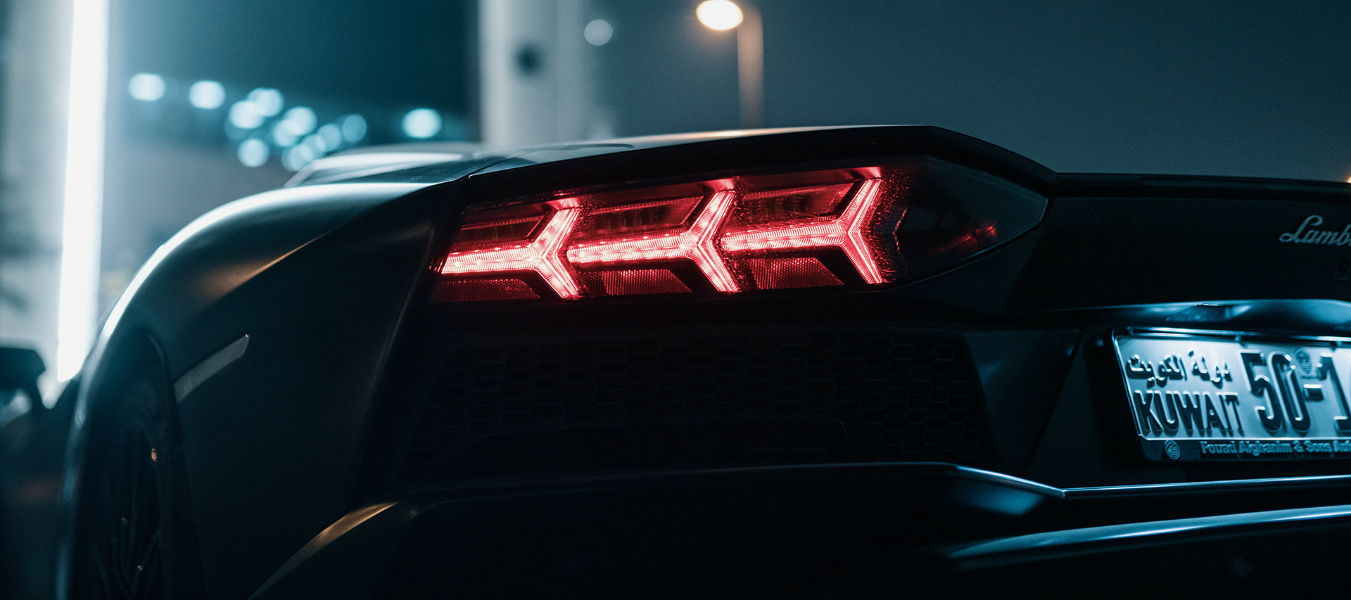 Rear taillight of a black supercar glowing red at night